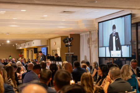 Audience seated at tables watching a speaker on a large projection screen at a Cleveland non-profit fundraiser event.