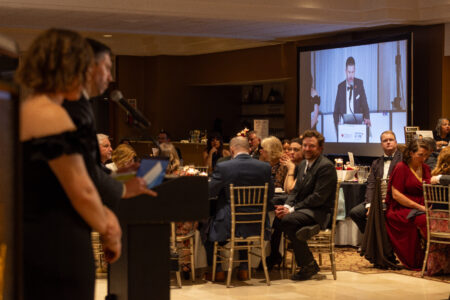 Speaker at the podium addressing guests during a Cleveland non-profit gala dinner presentation.